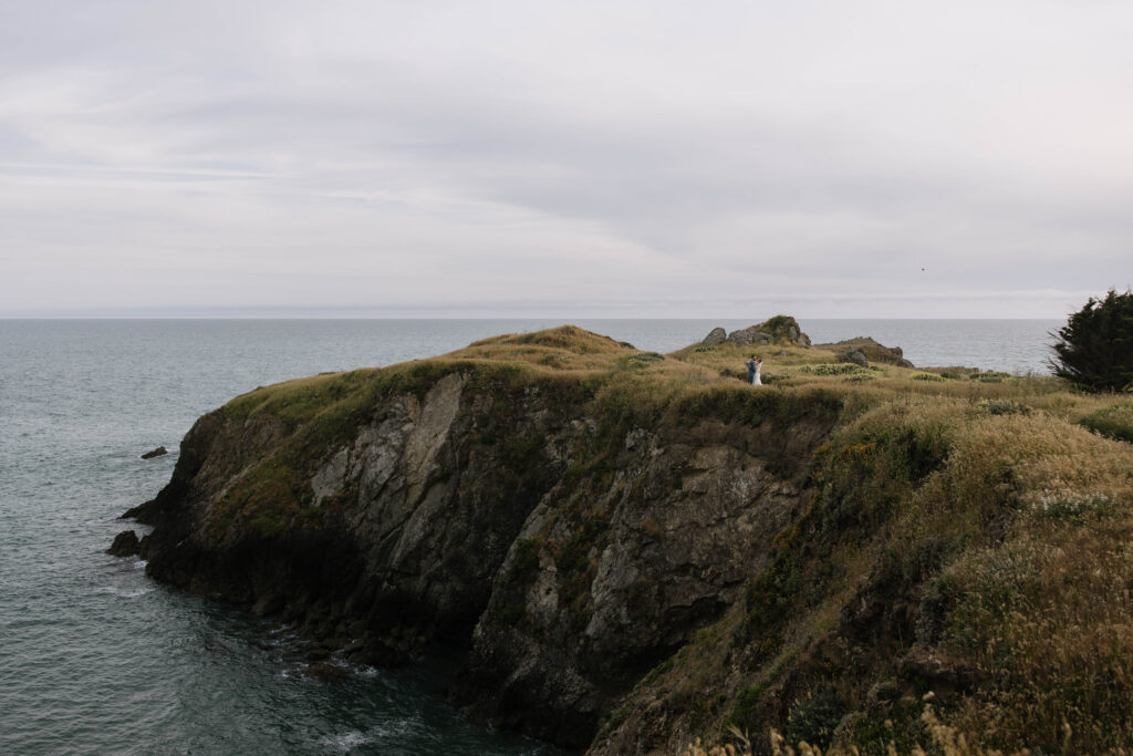Couple eloping on a coastal cliff in Northern California at sunset, overlooking the Pacific Ocean
